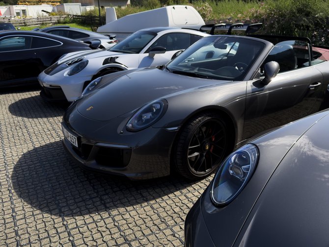 Cappuccino vor einer Reihe von Sportwagen auf einem Parkplatz mit Bergkulisse