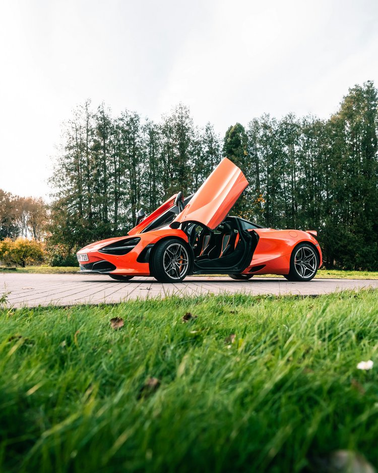 Oranger Sportwagen mit geöffneten Schmetterlingstüren auf Parkfläche vor Bäumen