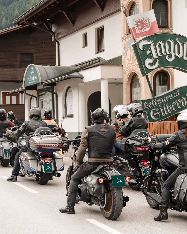 Gruppe von Motorradfahrern vor einem traditionellen Gasthaus in den Bergen