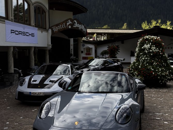 Mehrere Porsche vor einem Hotel in einem gepflasterten Hof vor bewaldeten Bergen