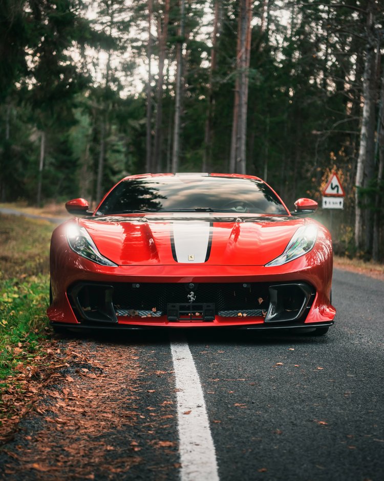 Rotes Sportauto mit weißen Streifen auf Waldstraße geparkt