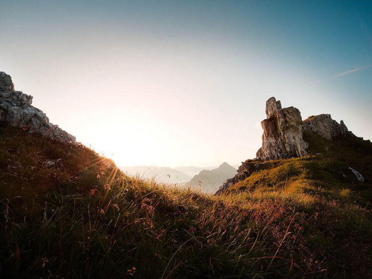 Sonnenaufgang über grasbewachsenen Bergen mit Felsen
