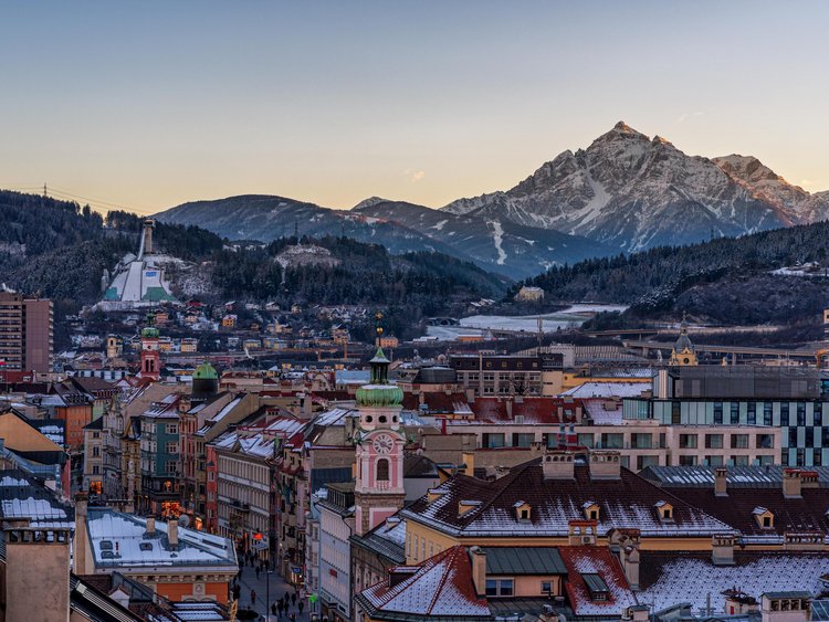Stadt mit historischen Gebäuden vor schneebedeckten Alpen im Sonnenuntergang