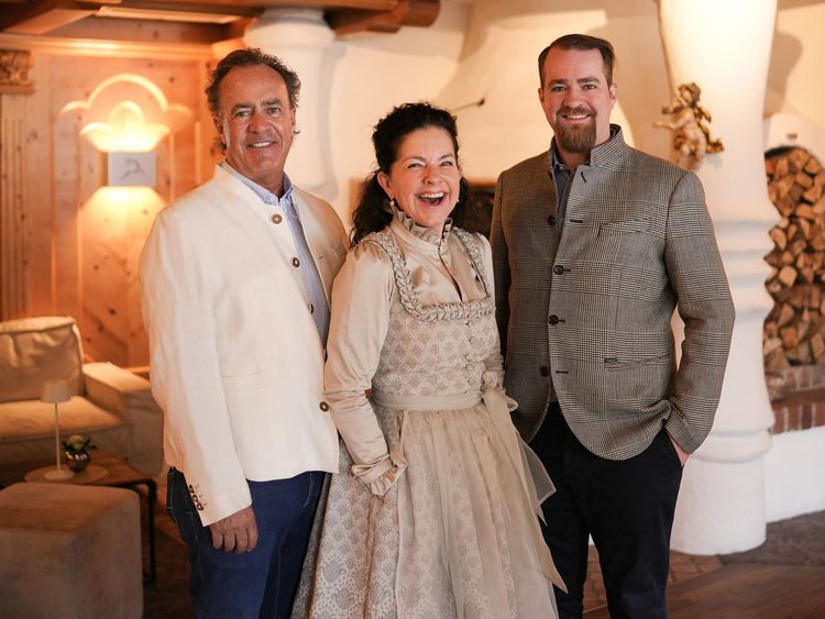 Three smiling people in traditional and modern clothes in a cozy room