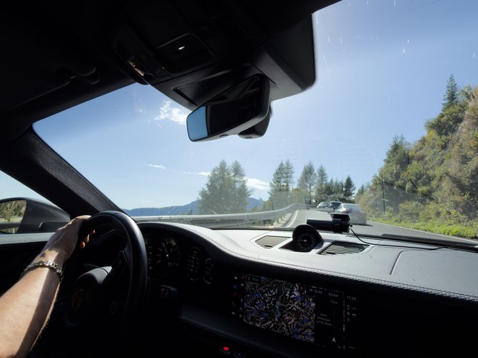 Blick aus dem Auto auf eine Bergstraße, während eine Hand das Lenkrad hält