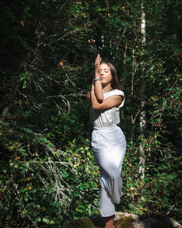 Frau macht Yoga-Pose in weißer Kleidung in grünem Wald