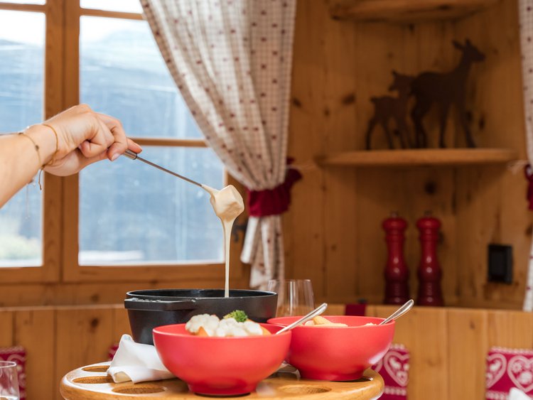 Einzigartig – die Jagdhof Fonduegondel Hand hält Käsefondue-Gabel mit Käse über einem schwarzen Topf