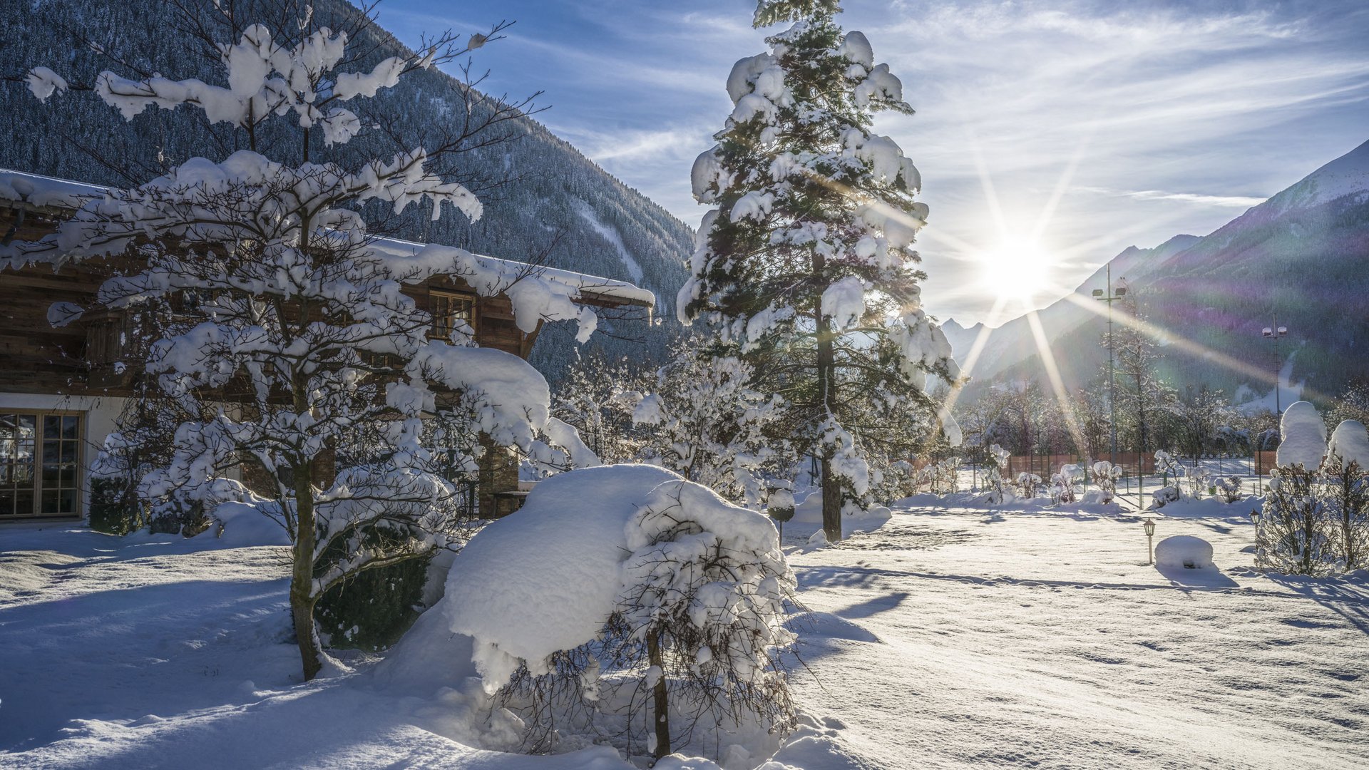 Welcome to the only 5-star hotel in Stubaital! Sunrise over snow-covered winter garden with trees and mountains