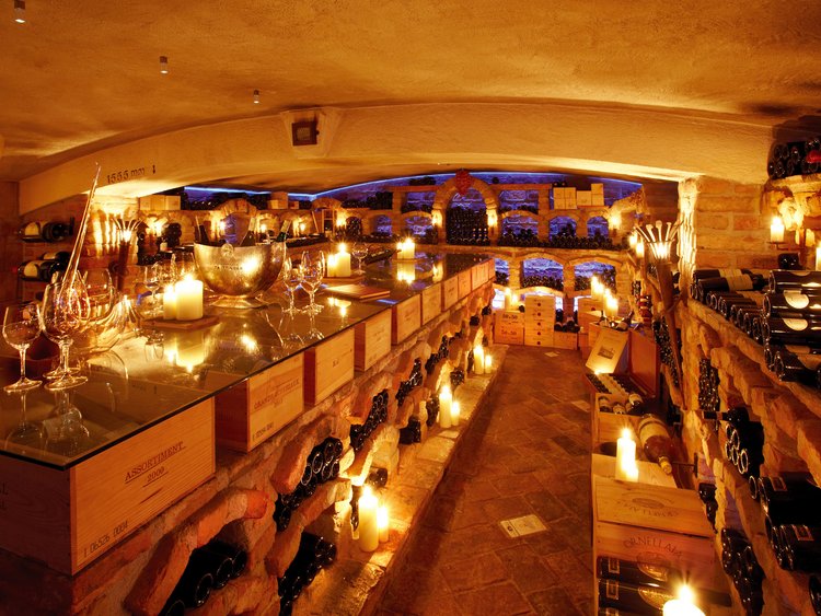 Weinkeller mit Weinflaschen, Kerzenlicht und Gläser auf einem Glastisch