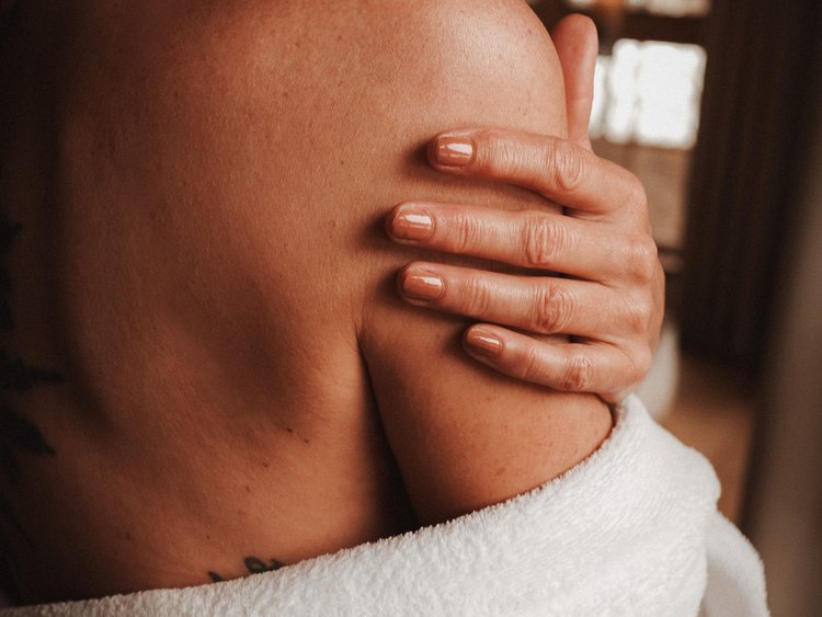 Frau hält ihre Schulter mit weißem Bademantel im warmen Innenraum