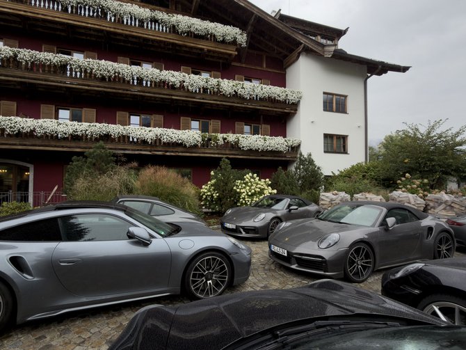 Alpenhotel mit blumengeschmückten Balkonen und Sportwagen auf dem gepflasterten Parkplatz