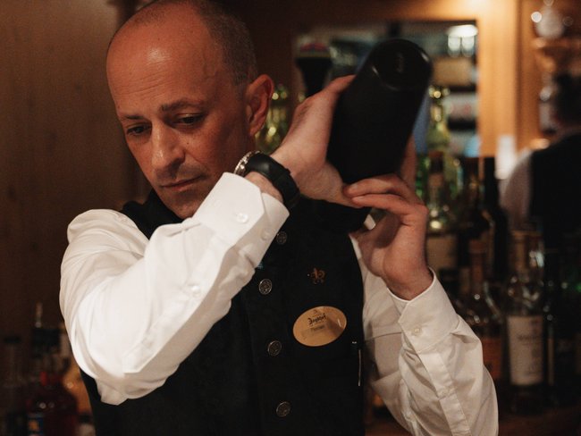 Discover the Jagdhof, Stubaital, and Tyrol Bartender shaking cocktail shaker behind the bar in a restaurant