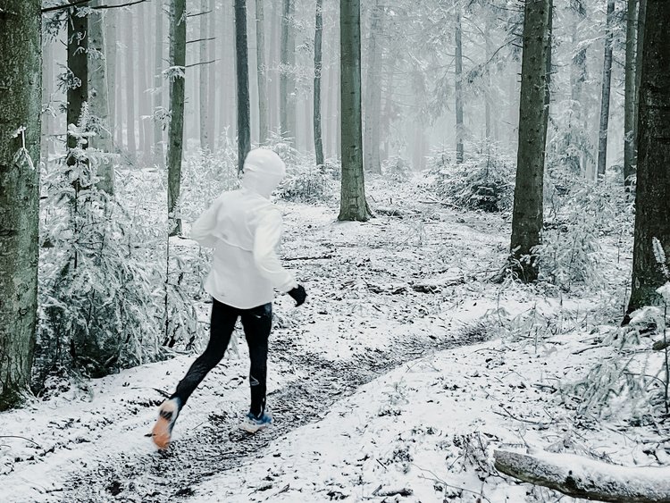 Person läuft auf schneebedecktem Waldweg zwischen Bäumen im Winter