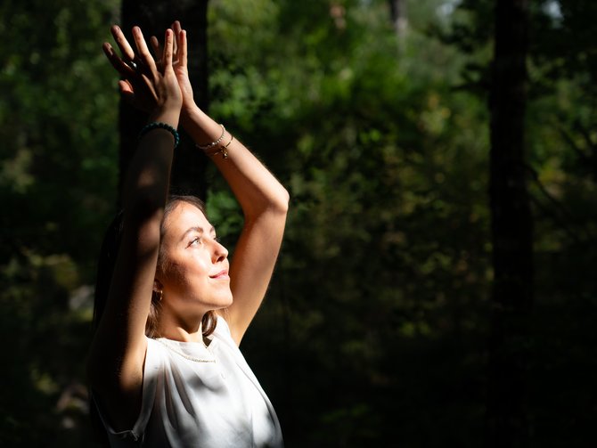 Frau in weißem Shirt beim Yoga im Wald mit erhobenen Händen