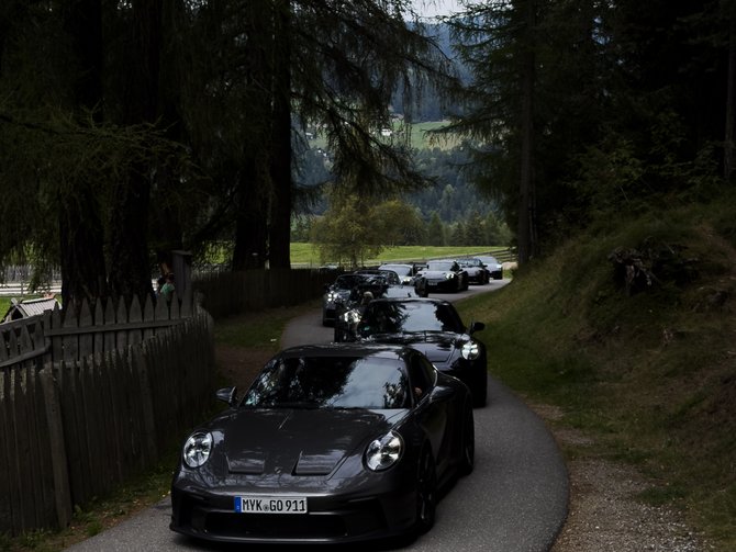 Mehrere schwarze Sportwagen fahren auf einer schmalen Straße durch einen Wald