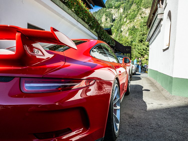 Roter Sportwagen hinten geparkt vor weißem Haus mit Bergen im Hintergrund