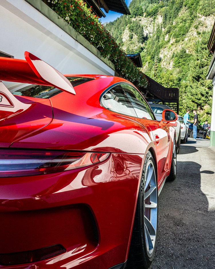 Red sports car parked behind white house with mountains in background