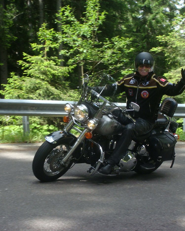 Motorradfahrer winkt auf kurviger Straße vor Wald
