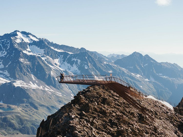 Discover the Jagdhof, Stubaital, and Tyrol Viewing platform with people on rocky peak against snowy alpine mountain backdrop