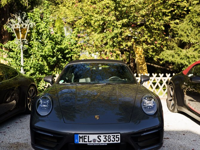 Schwarzer Porsche vor üppigem Grün auf einem gepflasterten Parkplatz