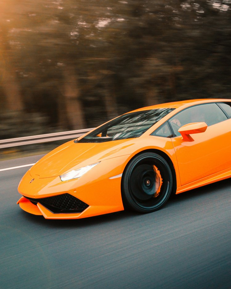 Oranger Sportwagen fährt auf der Straße bei Sonnenuntergang