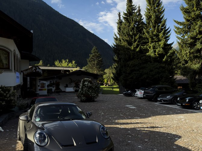 Dunkler Sportwagen auf dem Hotelparkplatz vor Tannen und einer bewaldeten Bergkulisse