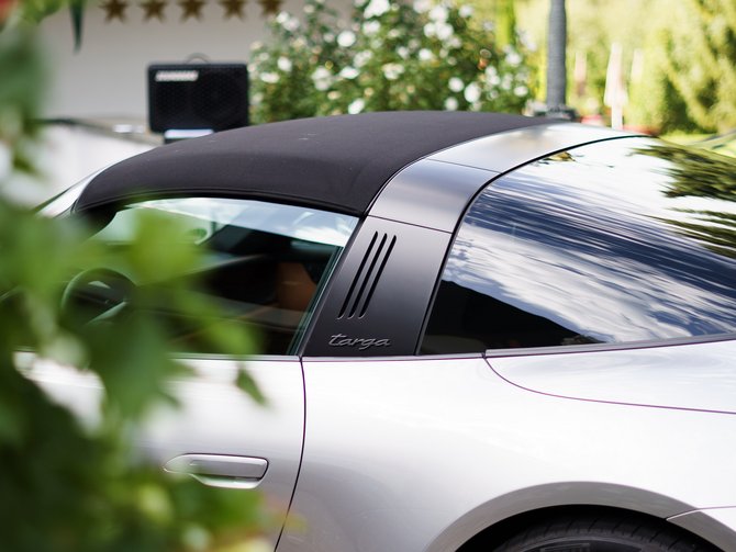 Silberner Porsche Taycan vor einem Gebäude mit fünf Sternen, umgeben von Blumen und Bergkulisse