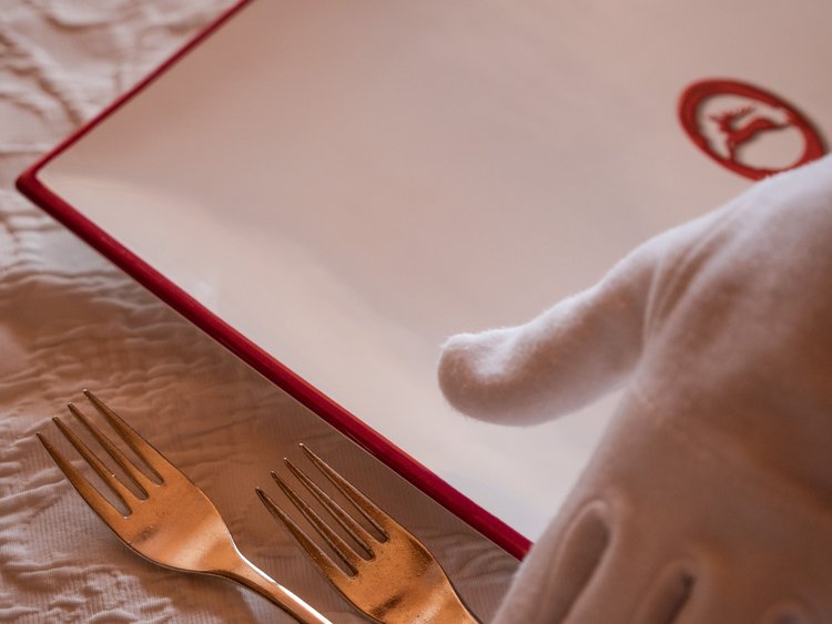 Discover the Jagdhof, Stubaital, and Tyrol White gloves place two golden forks on a white quilted cloth next to a red book