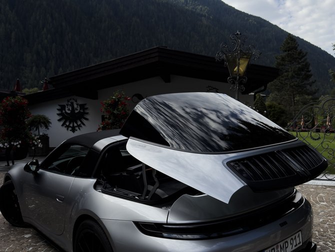 Silberner Sportwagen mit geöffneter Heckklappe vor einem Haus in den Bergen