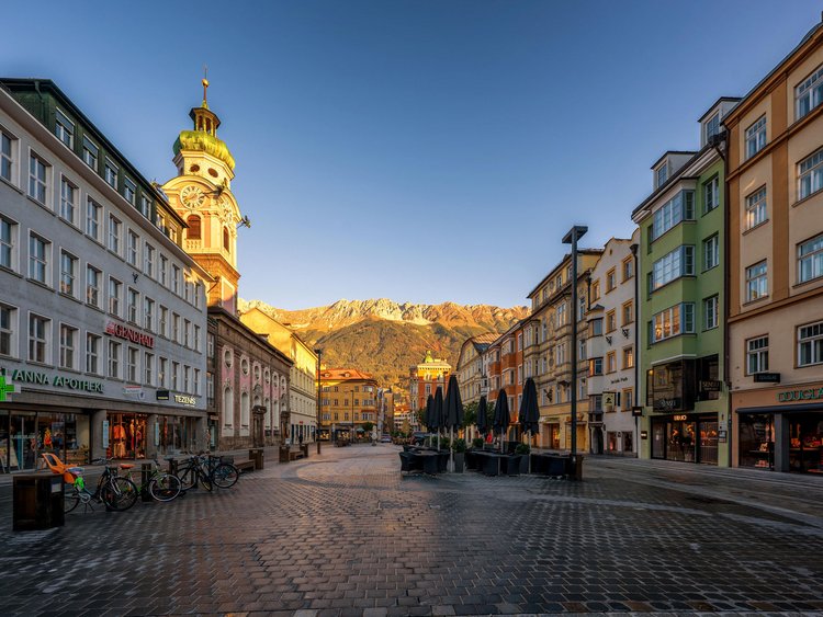 Abendliche Fußgängerzone mit historischer Uhrenturm und Bergpanorama