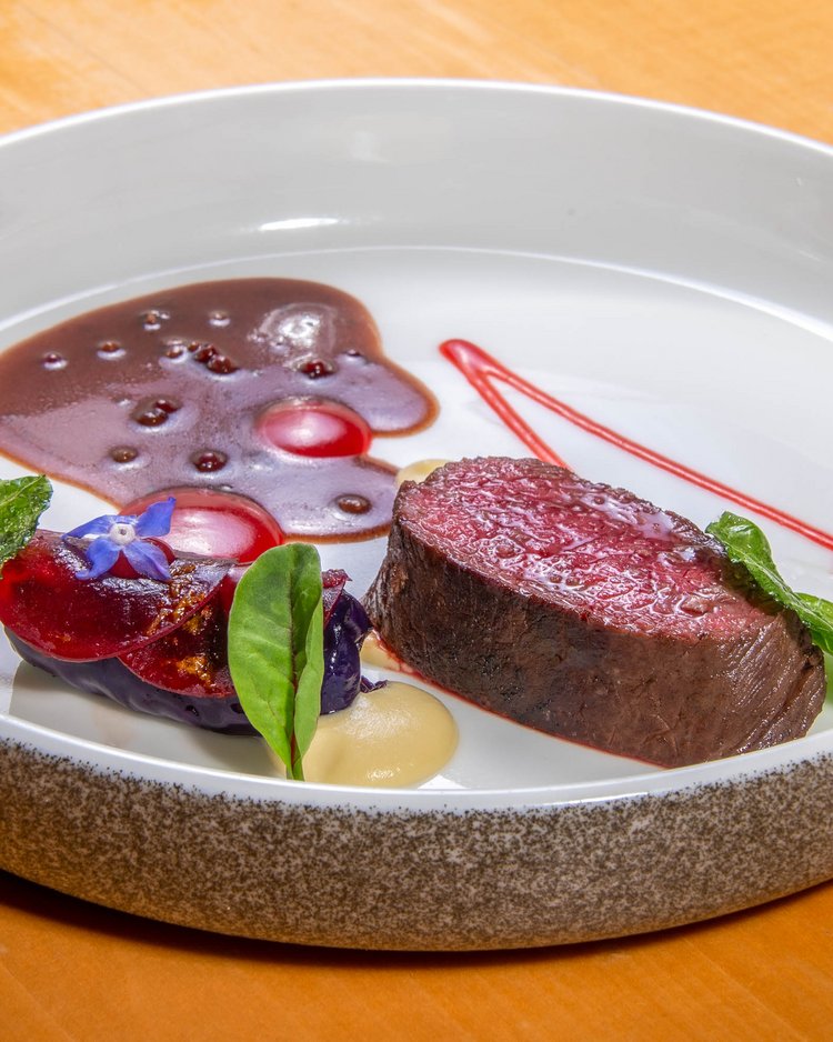Fein angerichtetes Fleischgericht mit Sauce und Kräutern auf weißem Teller