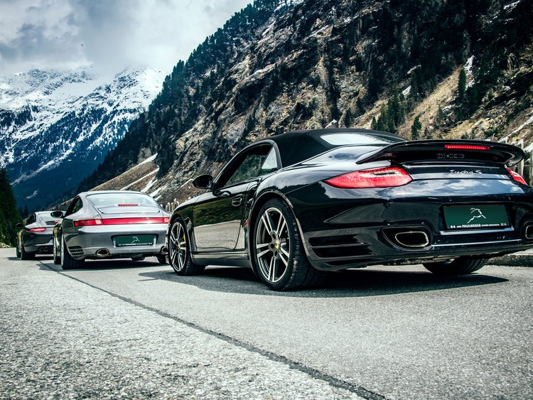Drei Porsche Sportwagen in Berglandschaft mit Schnee auf den Gipfeln