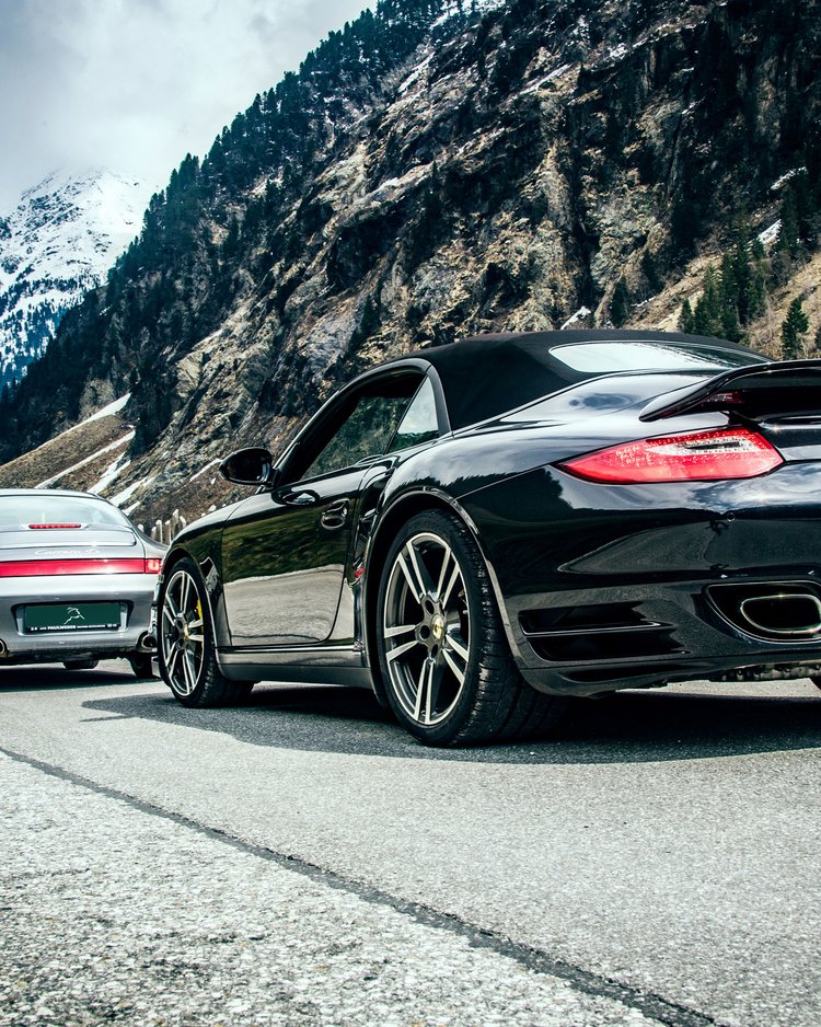 Drei Porsche Sportwagen in Berglandschaft mit Schnee auf den Gipfeln