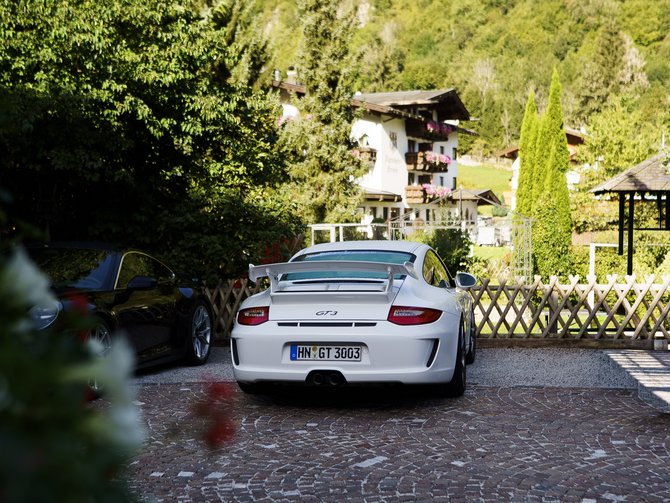 Weißer Sportwagen auf einem gepflasterten Parkplatz vor einem Haus in den Bergen