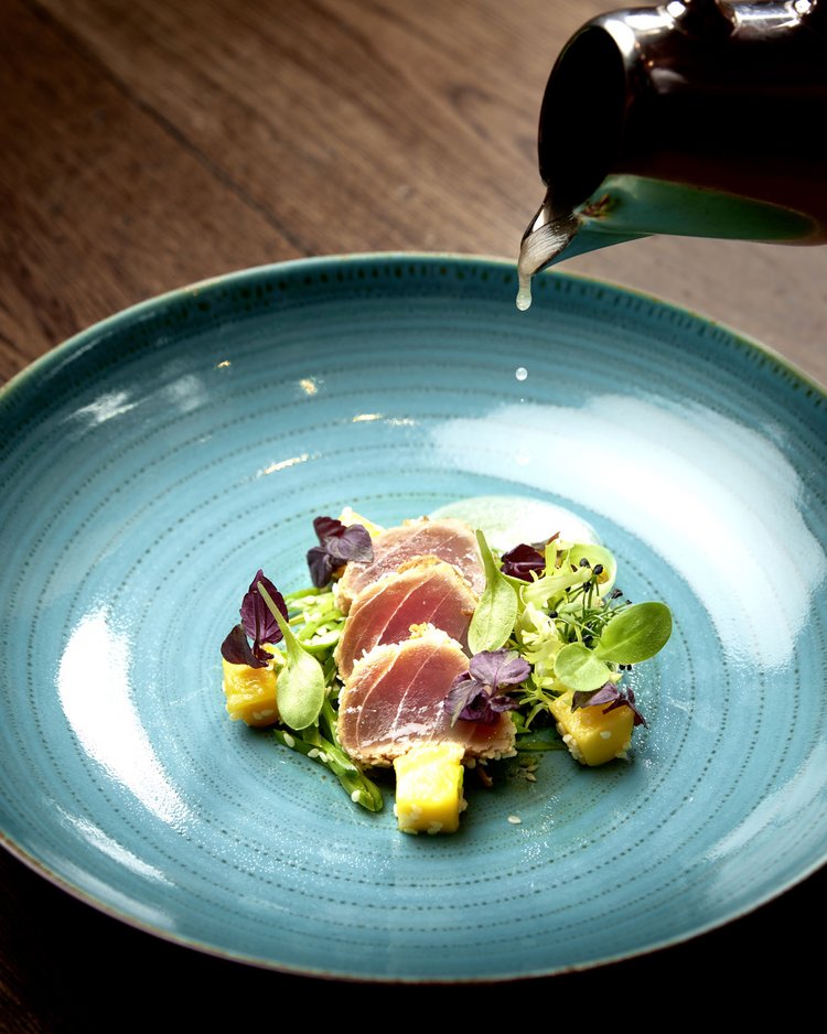 Fein angerichtete Vorspeise mit rohem Fisch, Mango und Blattsalat auf blauem Teller
