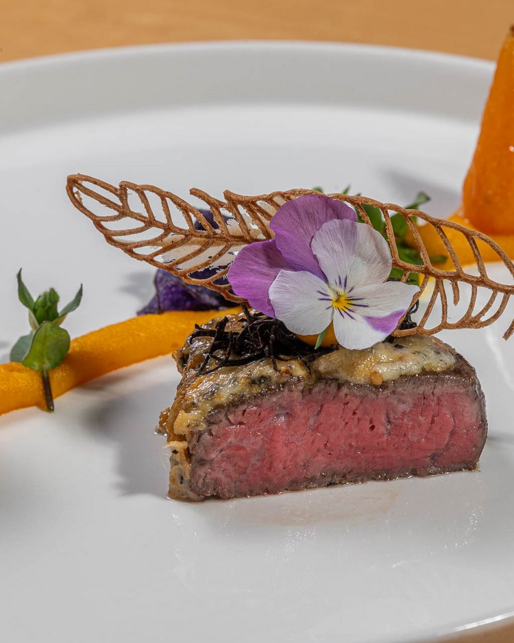 Gourmetgericht mit rosa gebratenem Fleisch, essbaren Blumen und feiner Dekoration