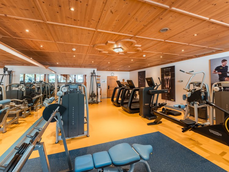 Innenansicht eines Fitnessraums mit Trainingsgeräten und Holzbalkendecke