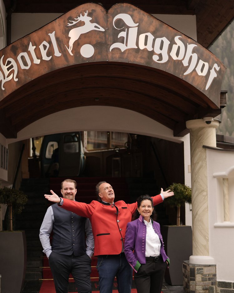 Drei Personen stehen vor dem Eingang des Hotels Jagdhof mit rotem Teppich